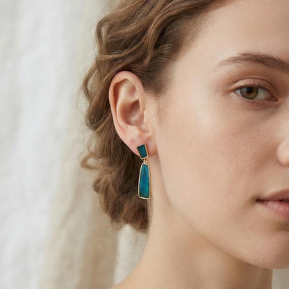 Model wearing the geometric drop earrings, showing the iridescent blue peacock feather inlay